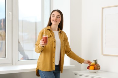 Photo of Beautiful young woman with delicious smoothie taking fruit at home
