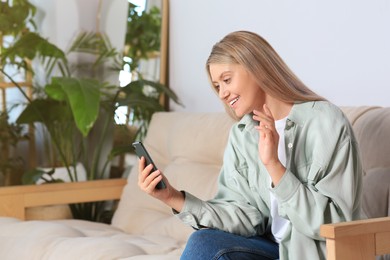 Woman with smartphone having video chat on sofa at home