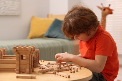 Photo of Little boy playing with wooden construction set at table in room. Child's toy