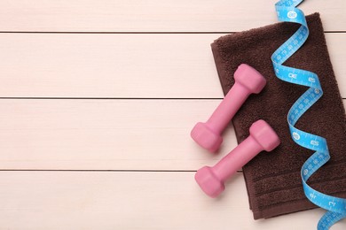 Photo of Dumbbells, measuring tape and towel on white wooden table, flat lay. Space for text
