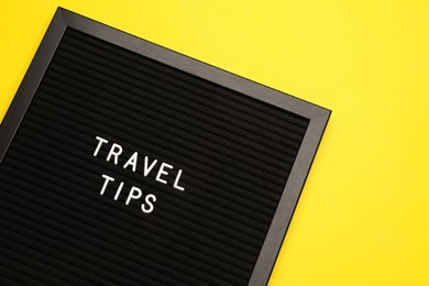 Photo of Black letter board with phrase Travel Tips on yellow background, top view