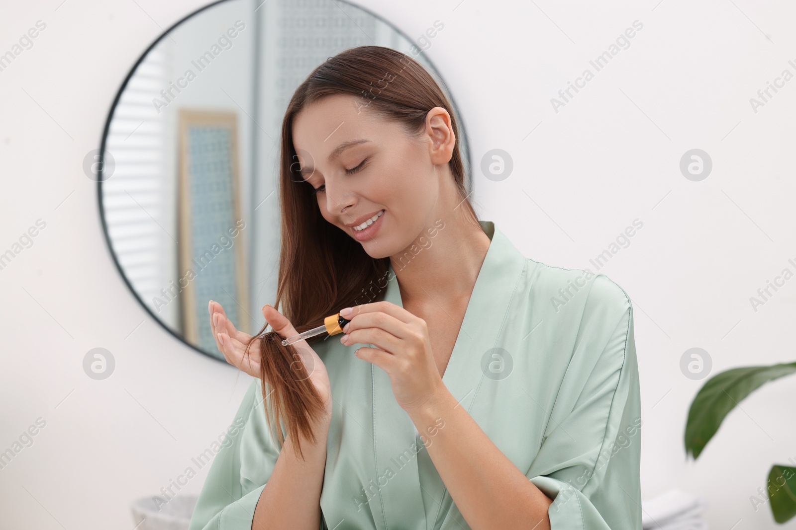 Photo of Beautiful woman applying serum onto hair indoors