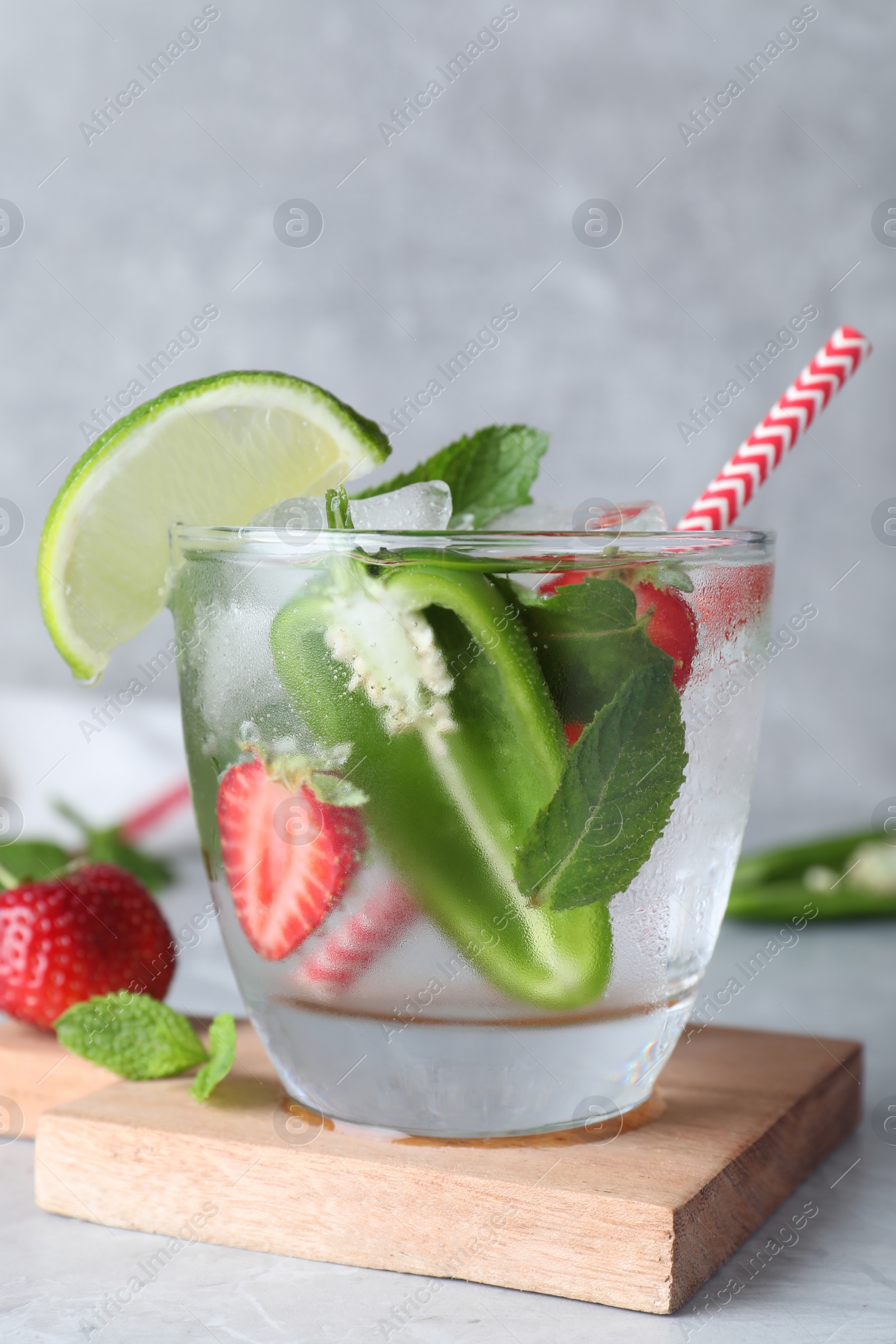 Photo of Spicy cocktail with jalapeno, strawberry, lime and mint on light grey table