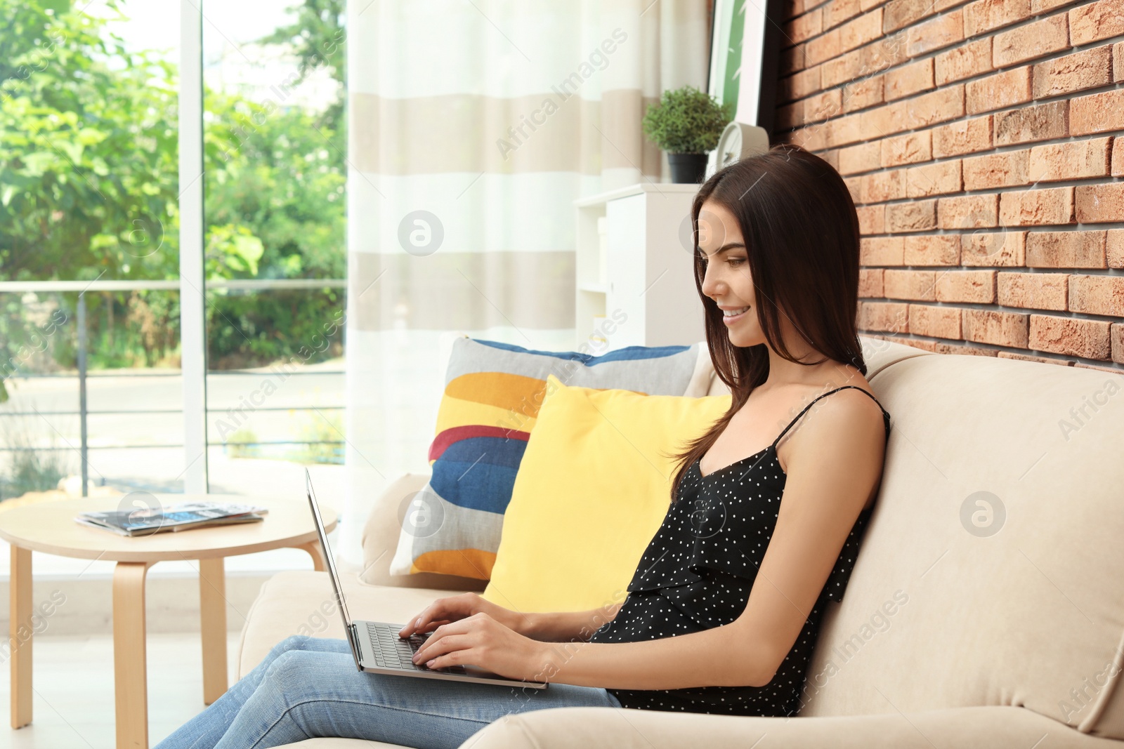 Photo of Young woman with modern laptop sitting on sofa at home