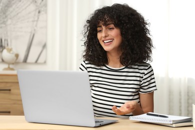 Happy woman having video chat via laptop at table in room