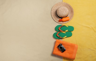 Beach towel, hat, sunscreen, camera and flip flops on sand, flat lay. Space for text