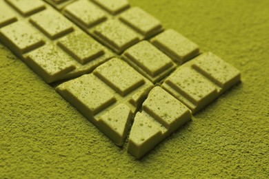 Photo of Pieces of tasty matcha chocolate bar on green powder, closeup