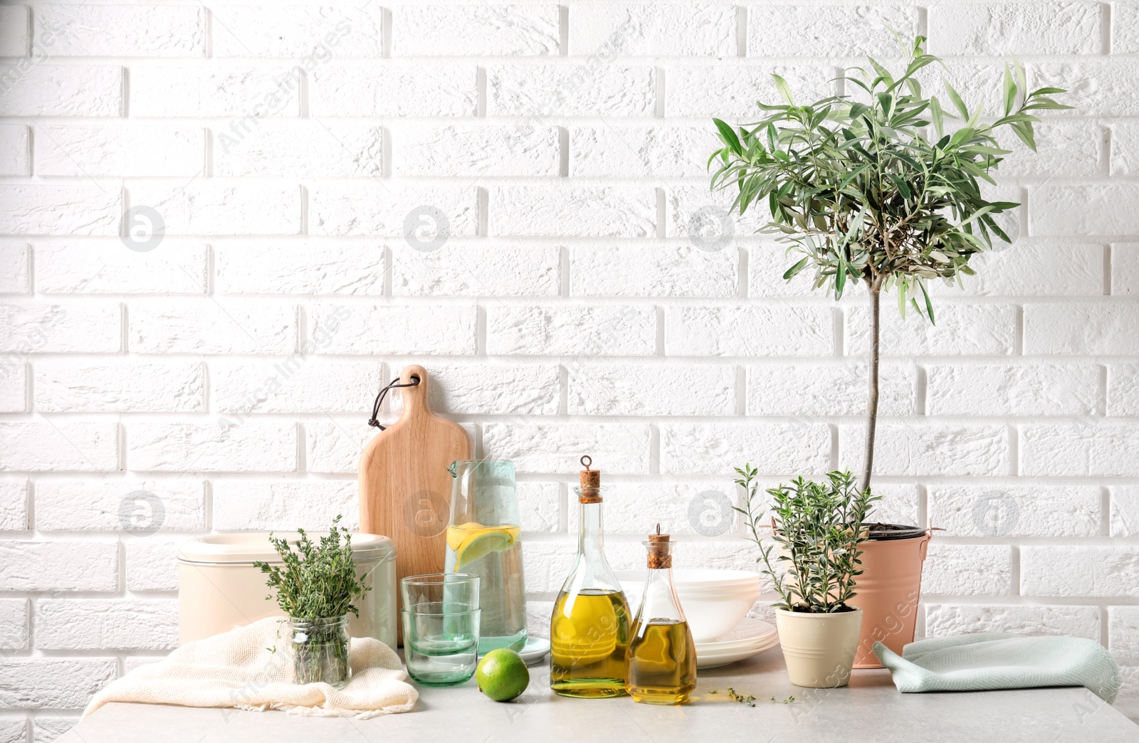 Photo of Fresh olive oil and kitchen utensils on table near brick wall