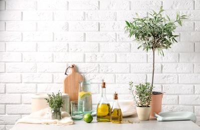 Fresh olive oil and kitchen utensils on table near brick wall