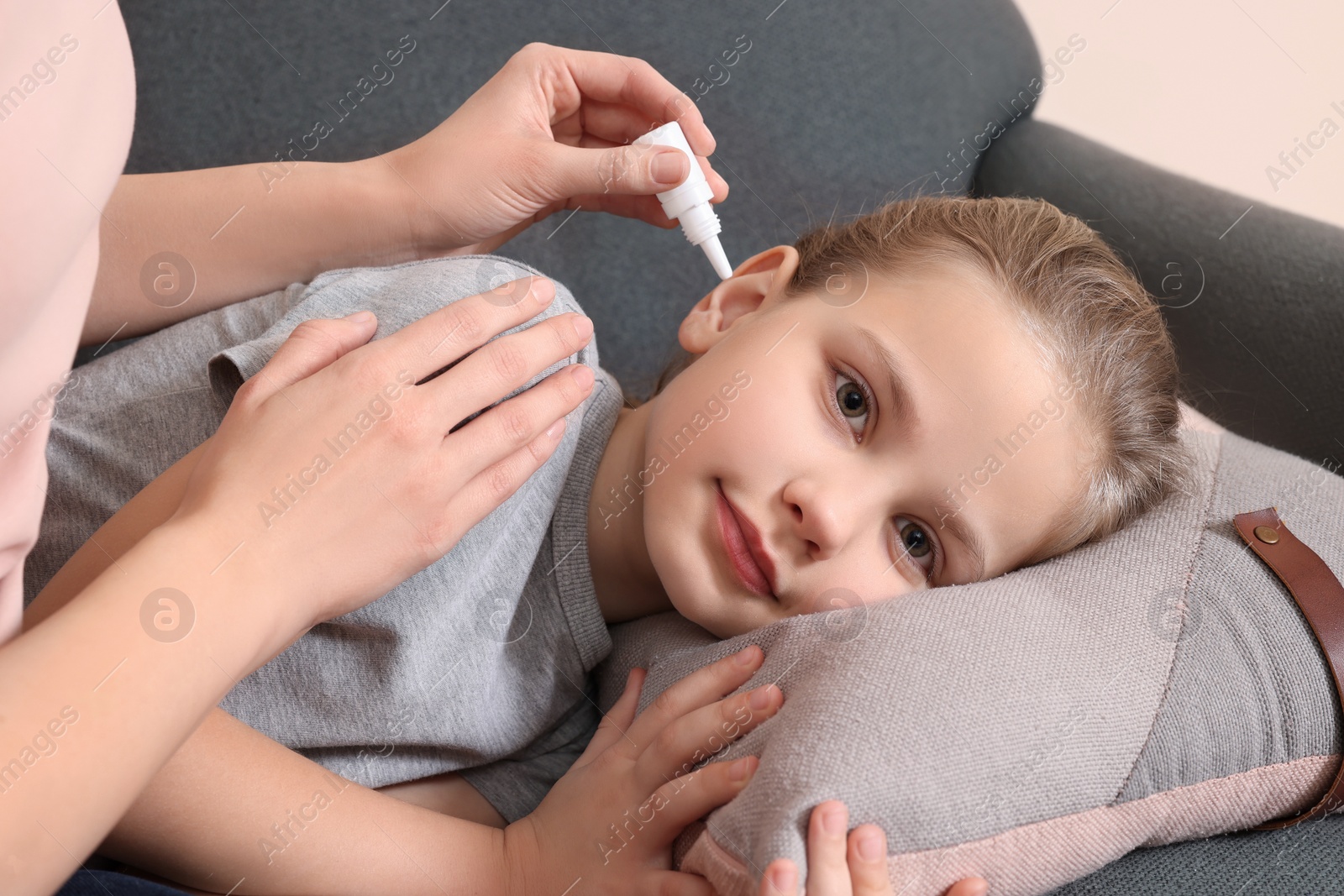 Photo of Mother dripping medication into daughter's ear in living room