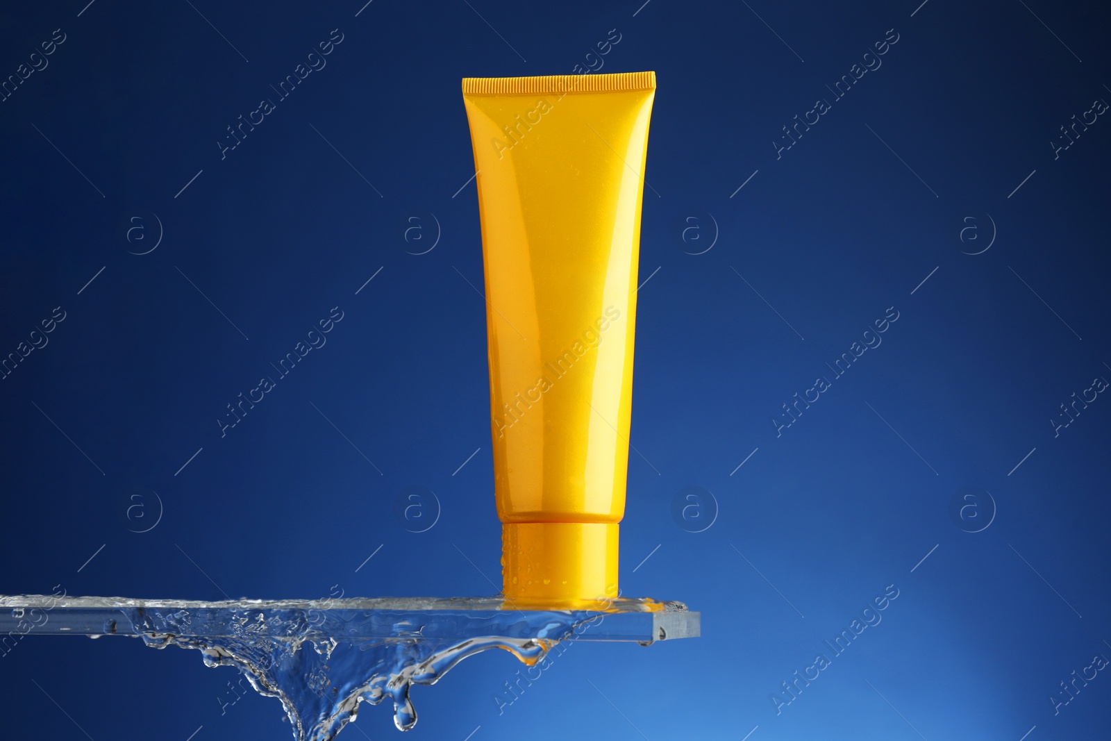 Photo of Moisturizing cream in tube on glass with water drops against blue background. Space for text