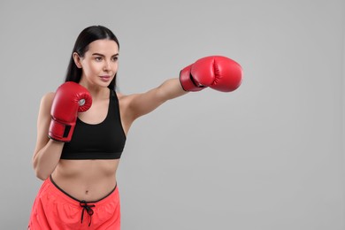 Photo of Beautiful woman in boxing gloves training on grey background. Space for text