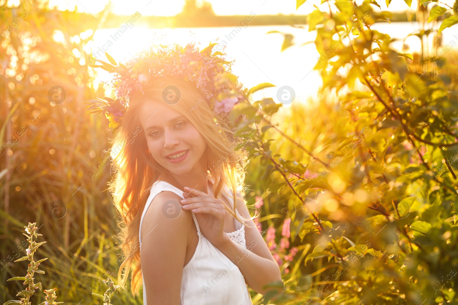 Photo of Young woman wearing wreath made of beautiful flowers outdoors on sunny day