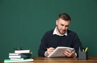 Portrait of young teacher at table against green background. Space for text