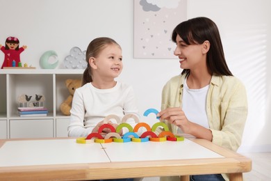Motor skills development. Mother helping her daughter to play with colorful wooden arcs at white table in room