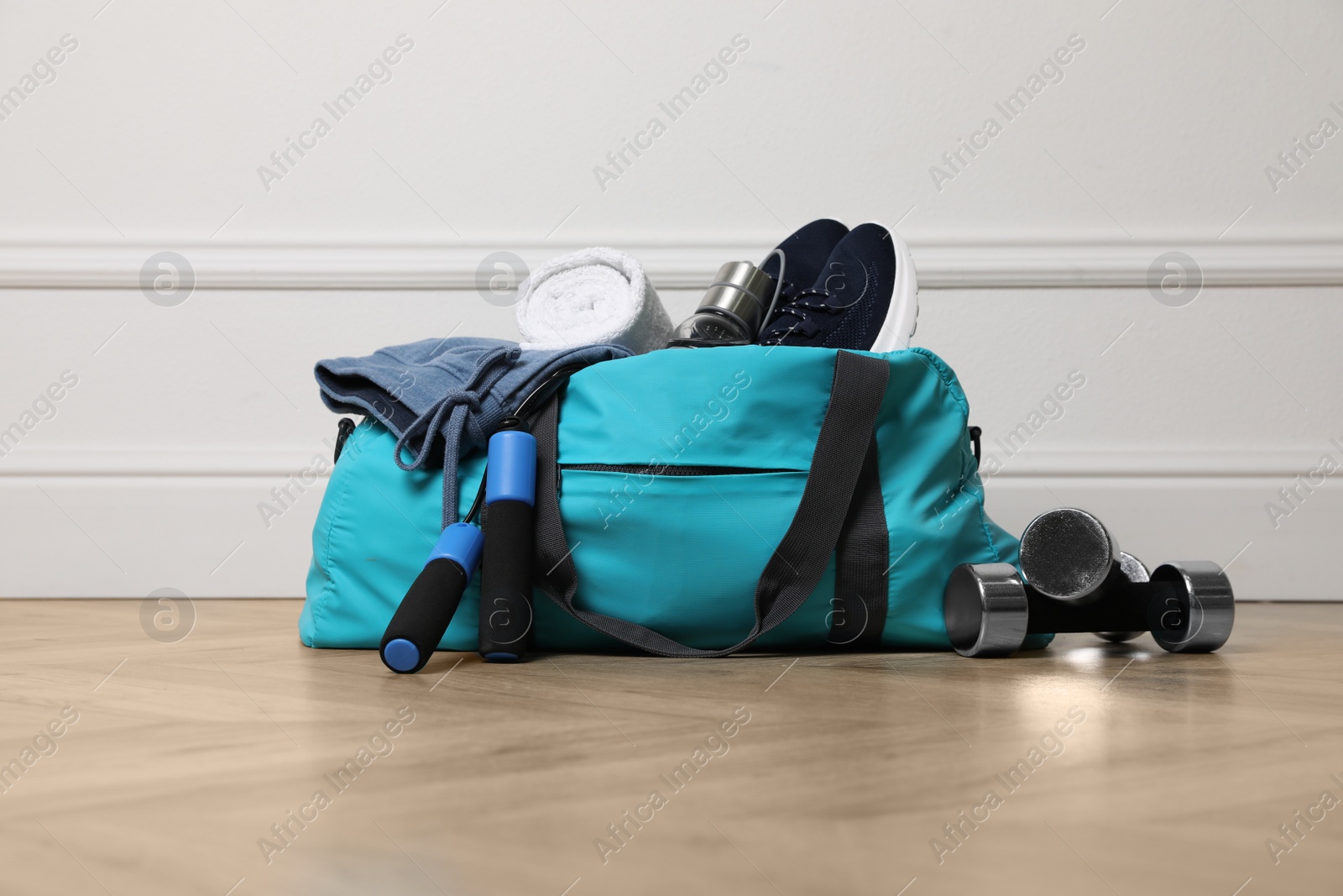 Photo of Blue gym bag with sports accessories on floor near white wall indoors