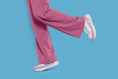 Woman wearing pair of new stylish sneakers on light blue background, closeup