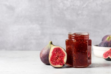 Photo of Jar of tasty sweet jam and fresh figs on white table. Space for text