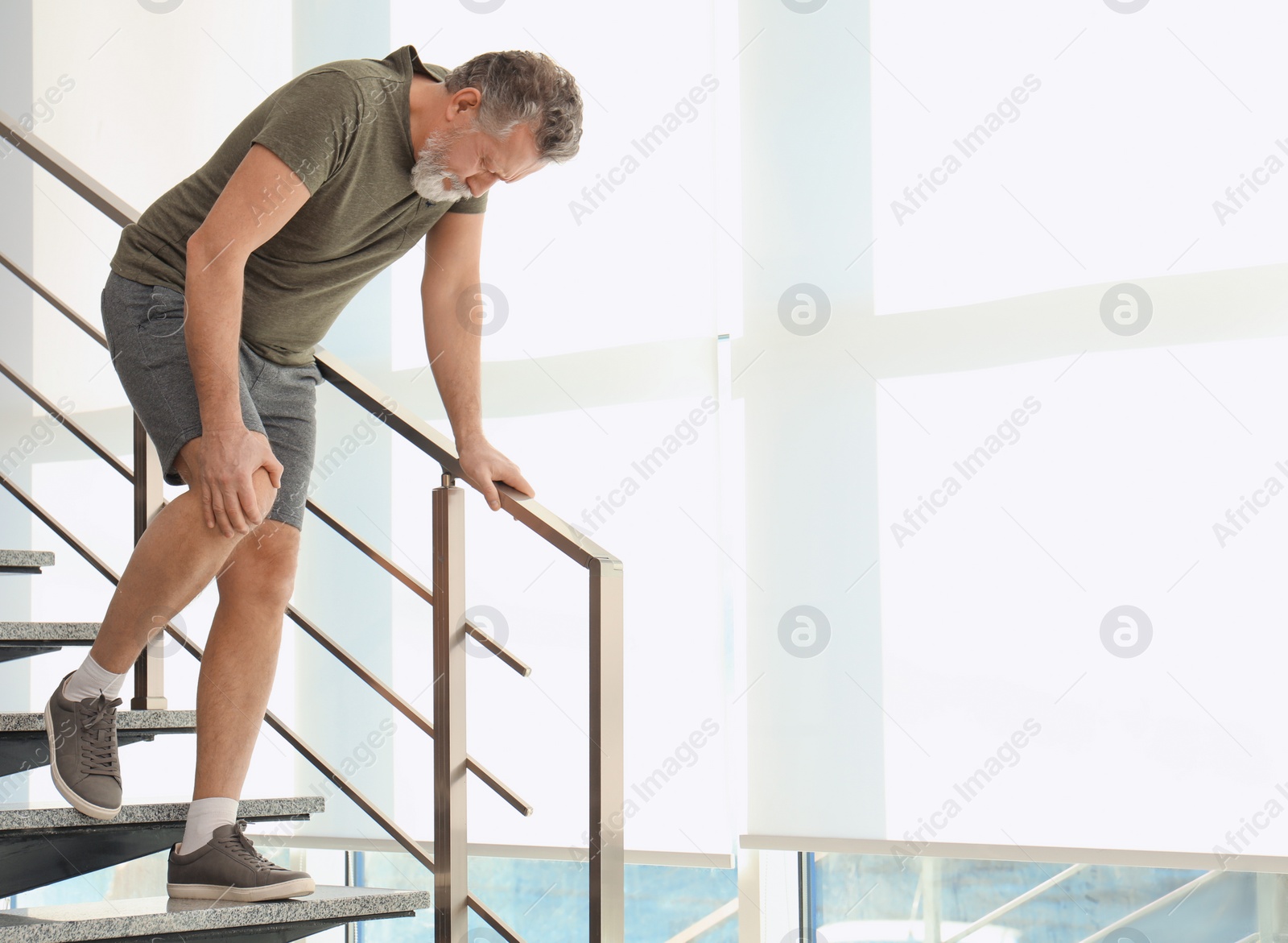 Photo of Senior man suffering from knee pain indoors. Space for text