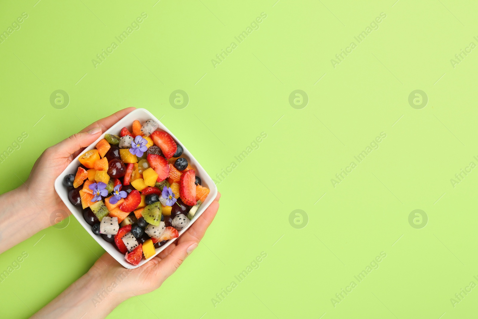 Photo of Woman with bowl of delicious exotic fruit salad on green background, top view. Space for text