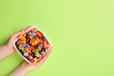 Woman with bowl of delicious exotic fruit salad on green background, top view. Space for text