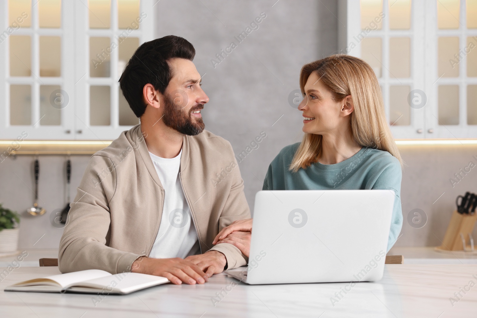 Photo of Happy couple with laptop at white table in kitchen