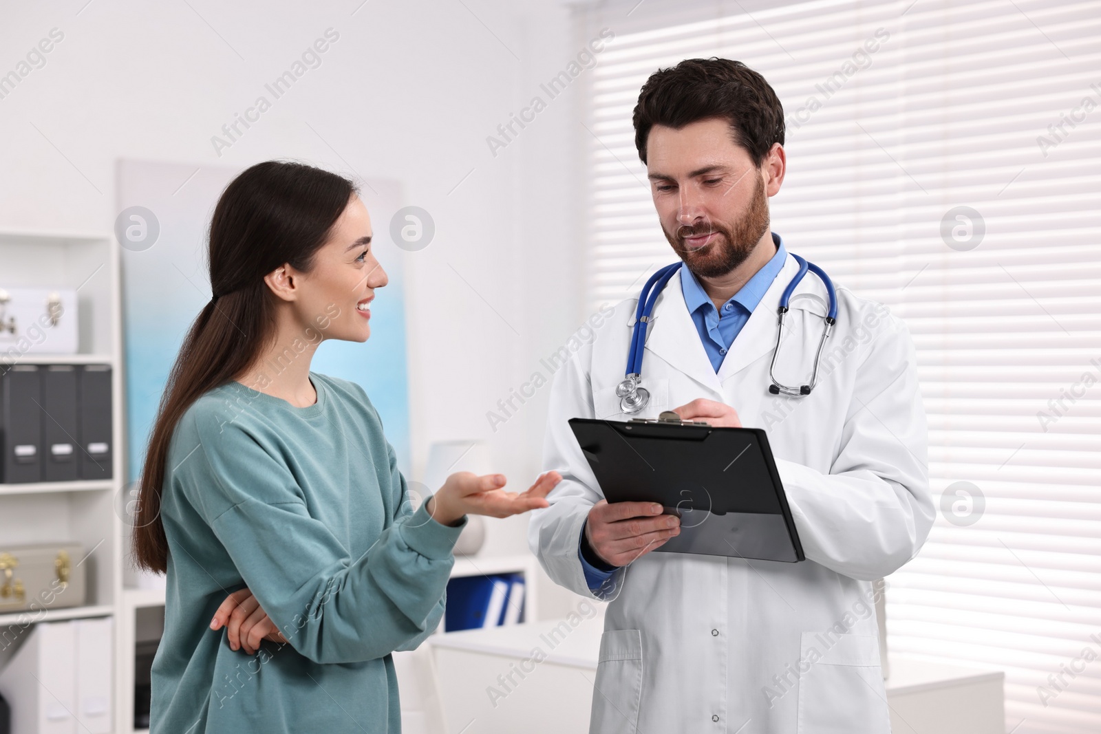 Photo of Doctor with clipboard consulting patient during appointment in clinic