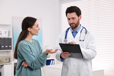 Doctor with clipboard consulting patient during appointment in clinic