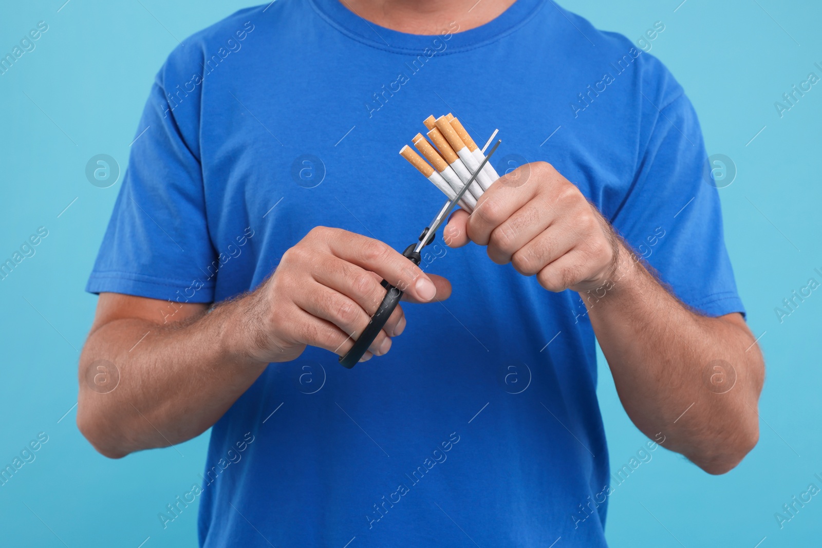 Photo of Stop smoking concept. Man cutting cigarettes on light blue background, closeup