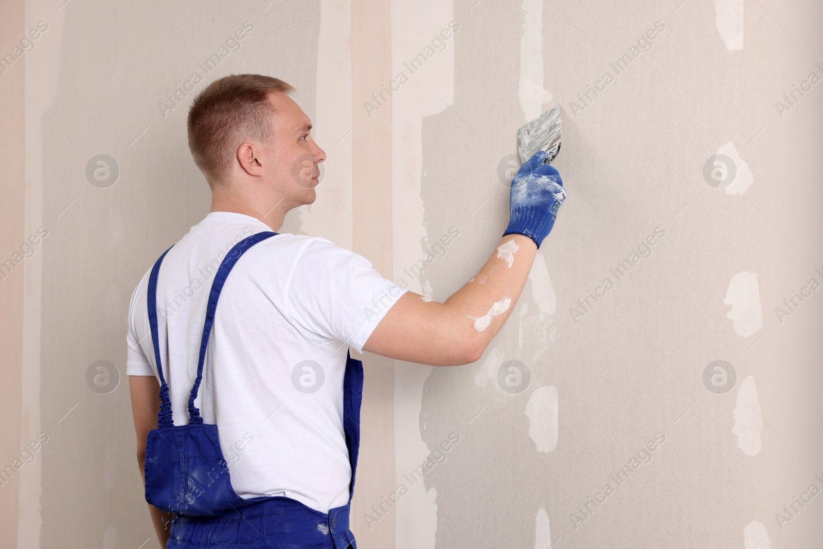 Photo of Man plastering wall with putty knife indoors. Home renovation