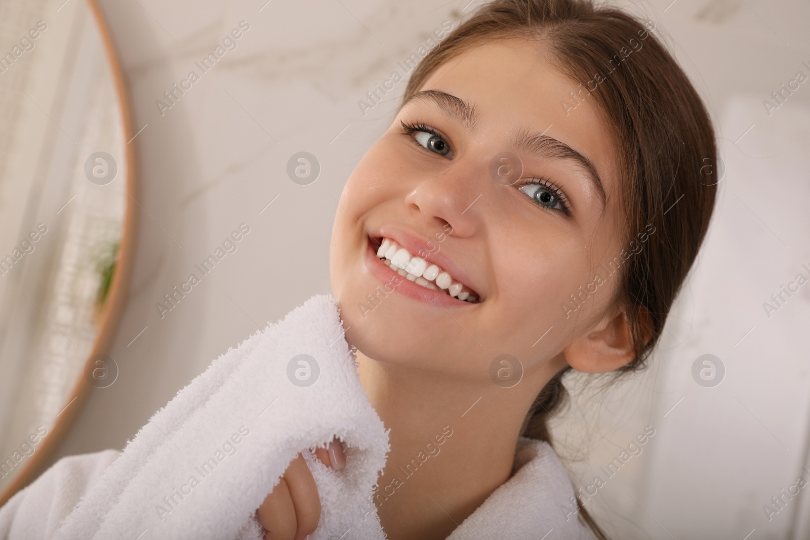 Photo of Beautiful teenage girl wiping face with towel at home, closeup