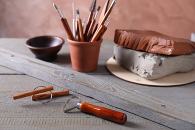 Set of different crafting tools and clay dishes on grey wooden table in workshop, closeup