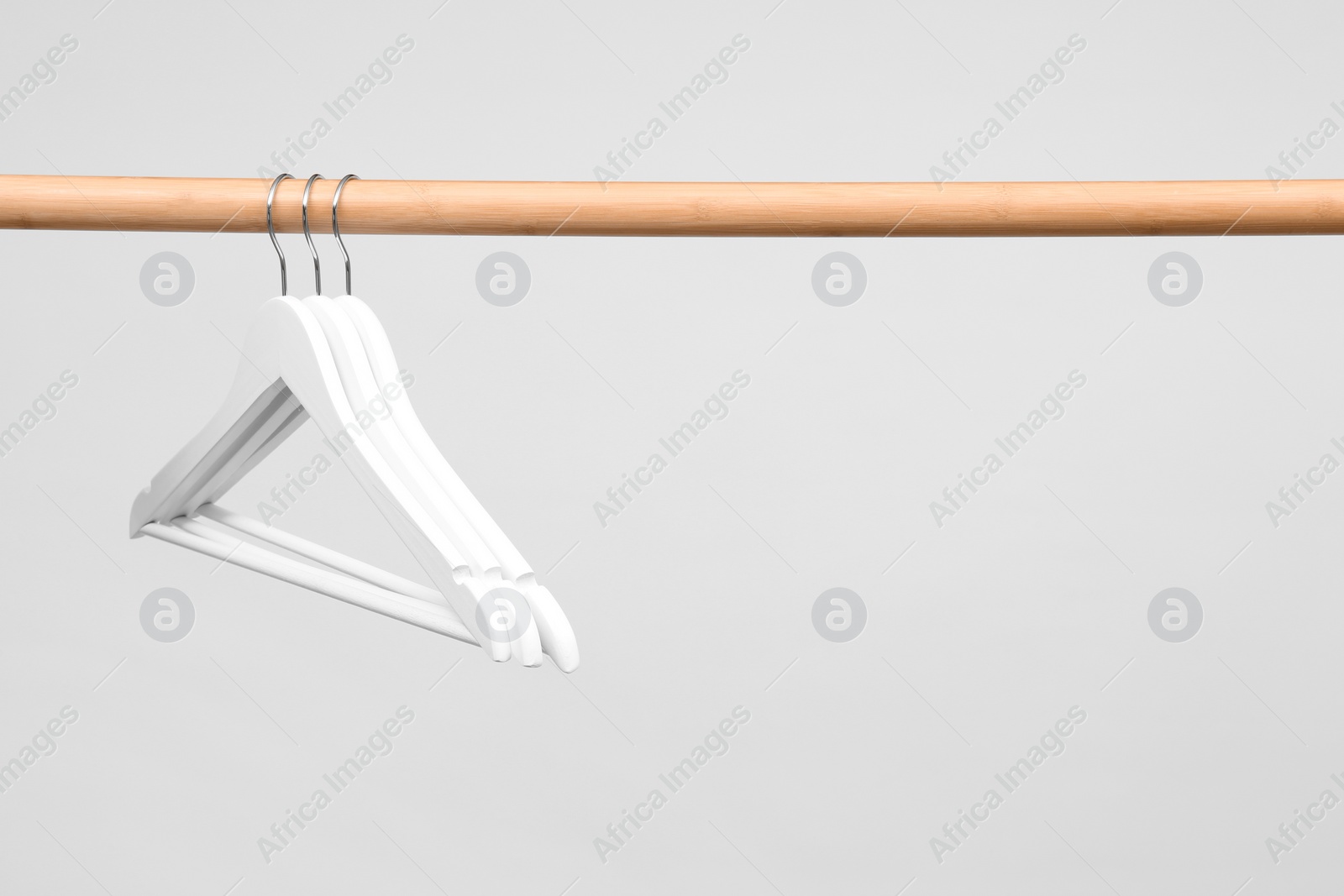 Photo of Empty clothes hangers on wooden rail against light background. Space for text