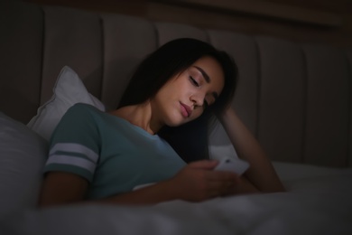Photo of Young woman with nomophobia using smartphone in bed at night. Insomnia concept