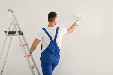 Man painting wall with white dye indoors, back view