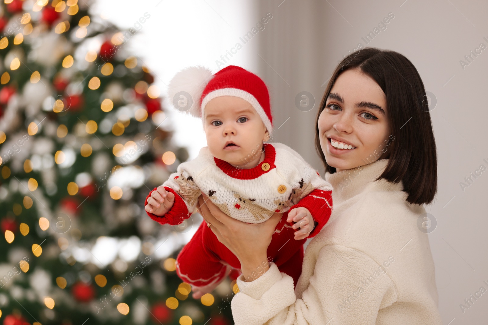 Photo of Happy young mother with her cute baby against blurred festive lights, space for text. Winter holiday