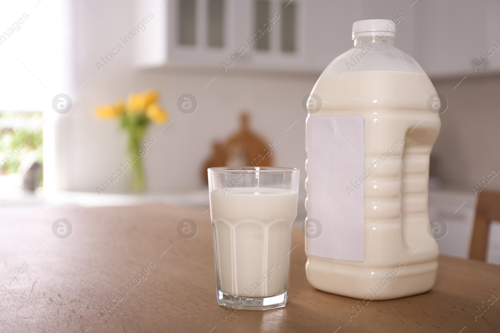 Photo of Gallon bottle of milk and glass on wooden table in kitchen. Space for text