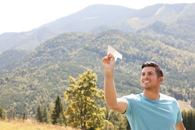 Man throwing paper plane in mountains on sunny day. Space for text
