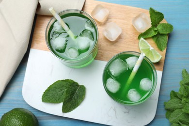 Photo of Delicious mint liqueur with green leaves and ice cubes on turquoise wooden table, flat lay