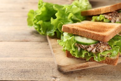 Photo of Delicious sandwiches with tuna, cucumber and lettuce leaves on wooden table, closeup. Space for text