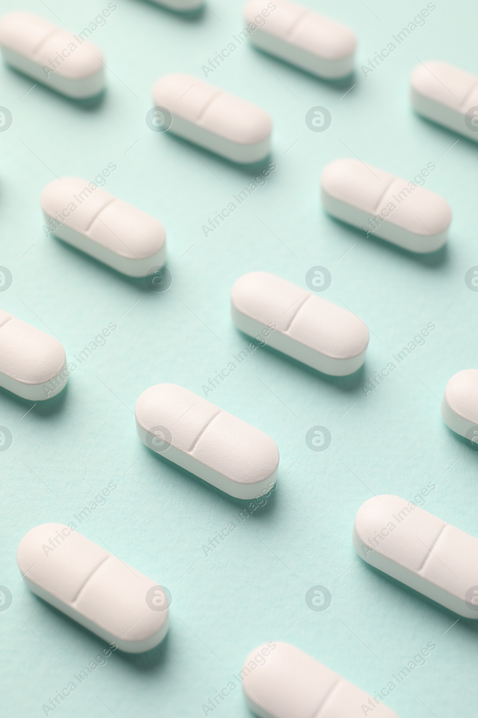 Photo of Many white pills on mint background, above view