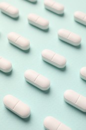 Many white pills on mint background, above view