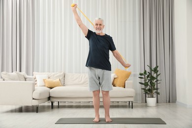 Photo of Senior man doing exercise with fitness elastic band on mat at home