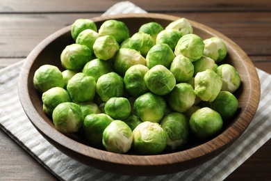 Photo of Bowl of fresh Brussels sprouts and napkin on wooden table