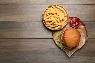 French fries, tasty burger and sauce on wooden table, flat lay. Space for text