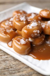 Tasty candies, caramel sauce and salt on wooden table, closeup