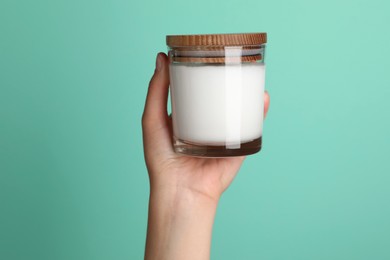 Woman holding jar of face cream on turquoise background, closeup