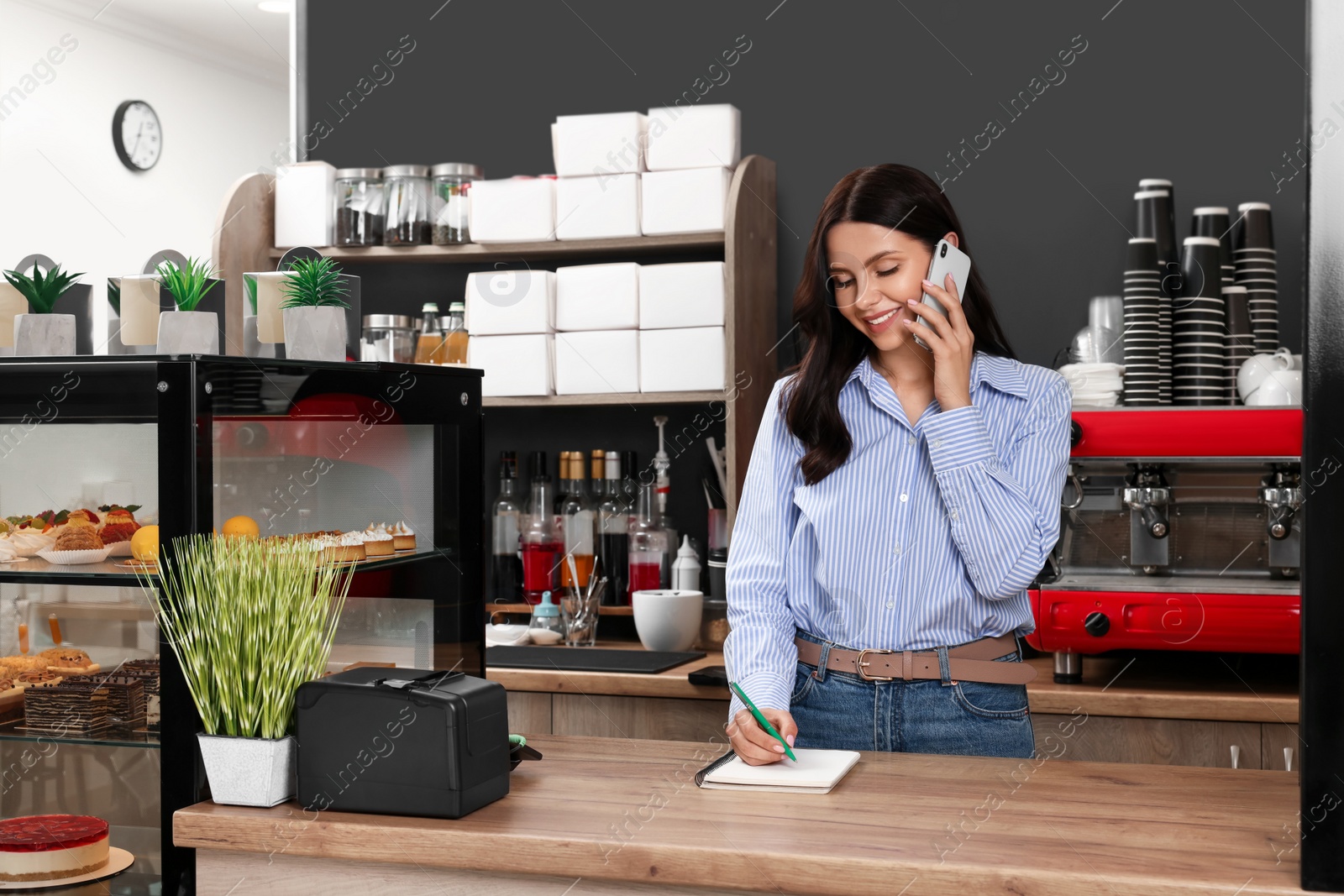 Photo of Business owner talking on phone while working near showcase in her cafe