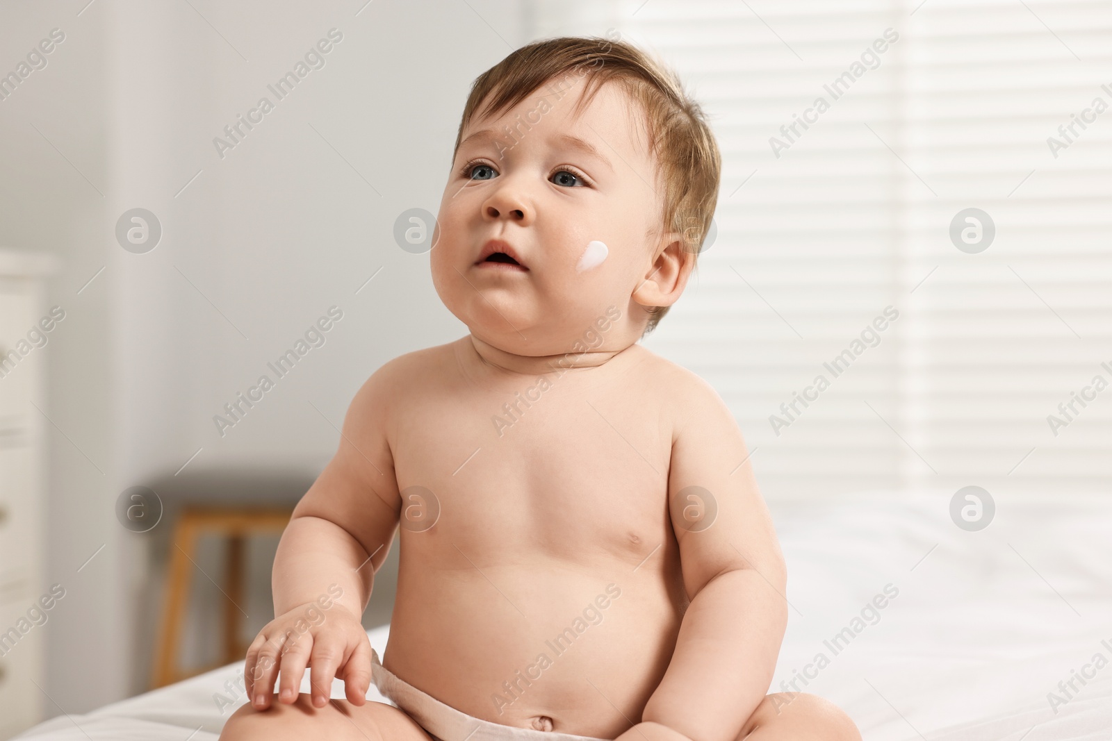 Photo of Cute little baby with moisturizing cream on face at home