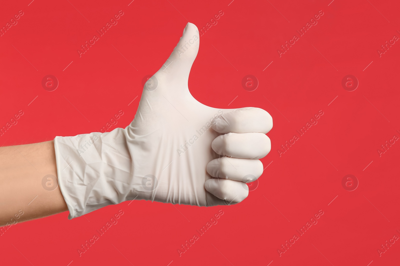 Photo of Person in medical gloves showing thumb up on red background, closeup of hand